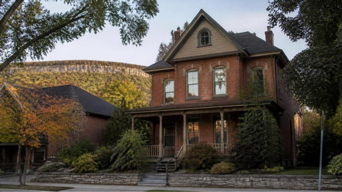 Century brick house with a front porch and the Niagara Escarpment behind